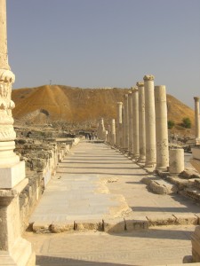 Il colonnato, un tempo coperto, che costituiva la passeggiata commerciale a Beit She’an. Sullo sfondo la grande collina di detriti probabilmente cerata nei secoli con lo scarico di rifiuti e macerie prodotti dalla città stessa.