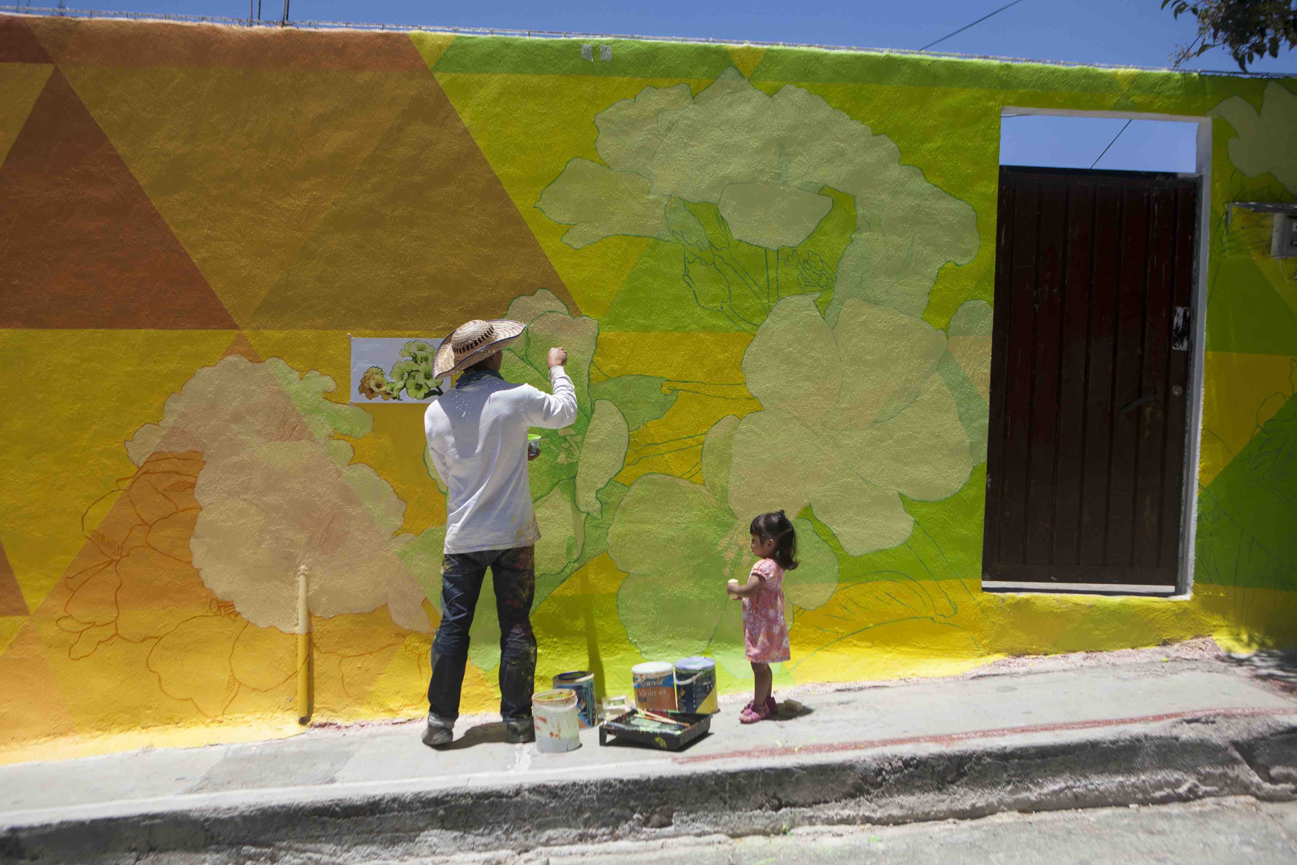 Carlos Duarte, del colectivo artístico Germen Colectivo, acompañado por la niña Regina Robles, pinta una parte del mural gigante en el barrio Palmitas, Pachuca, México, 30 de julio de 2015. (AP Foto/Sofia Jaramillo)